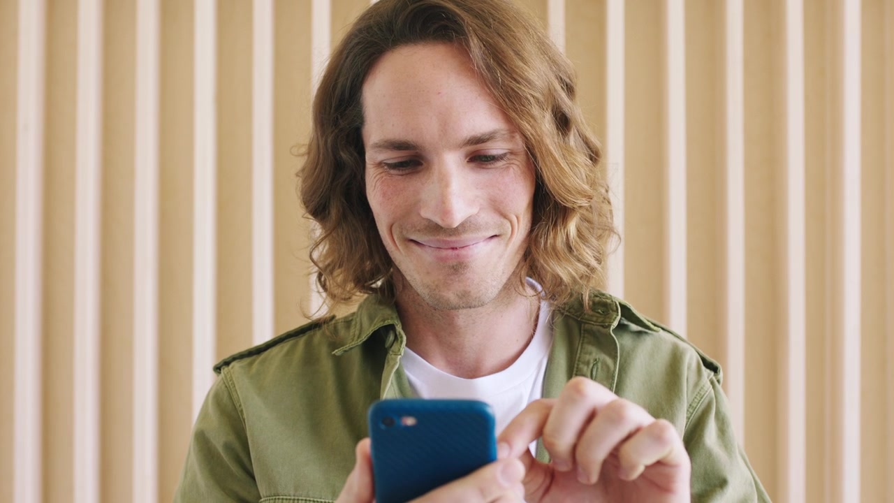 Giovane uomo che usa lo smartphone contro una parete di assi di legno
