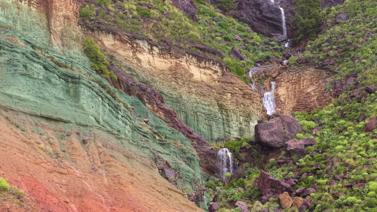 Formasi geologi berwarna-warni Los Azulejos de Veneguera di Gran Canaria dengan air terjun yang mengalir setelah hari hujan. Keajaiban alam.