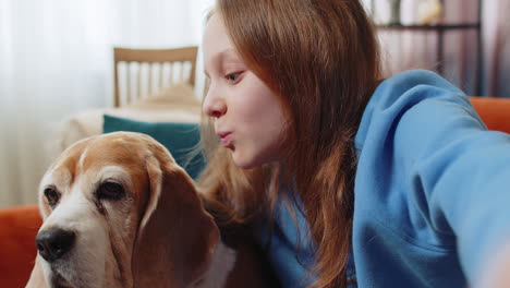 pov de una niña sonriente, un niño con un lindo perro beagle tomando selfies con su teléfono inteligente en la habitación de su casa.