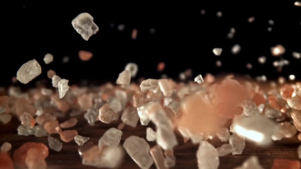 Cristalli di sale rosa dell'Himalaya che cadono su un tavolo di legno scuro al rallentatore