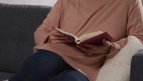 close up of muslim woman sitting on sofa at home reading or studying the quran