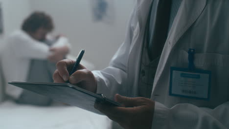 psychiatrist writing notes in hospital ward with distressed patient behind