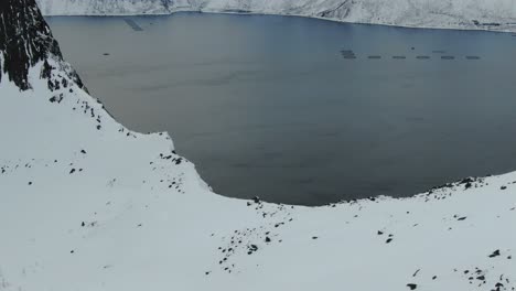 drone view in tromso area in winter flying over a snowy mountain and looking down the cliff into the fjord in segla, norway top view