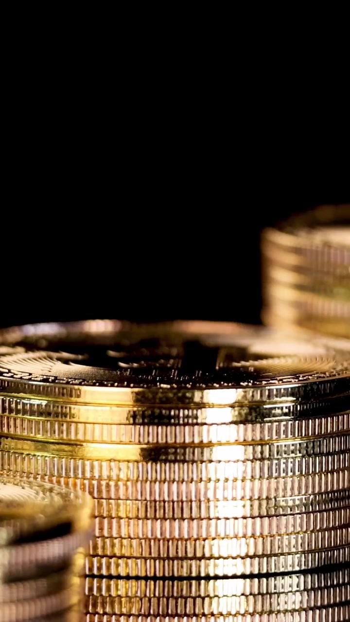 Camera rotates and zooms in on shiny gold coins, dramatic lighting, black background, macro view