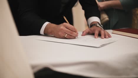 Groom-signing-the-marriage-document-in-the-town-hall,-close-up-writing