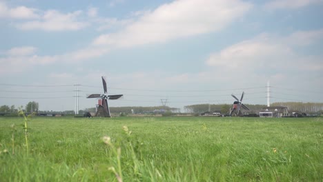 wide angle view of windmills at work in dutch countryside with lush green grassland in foreground on a windy day