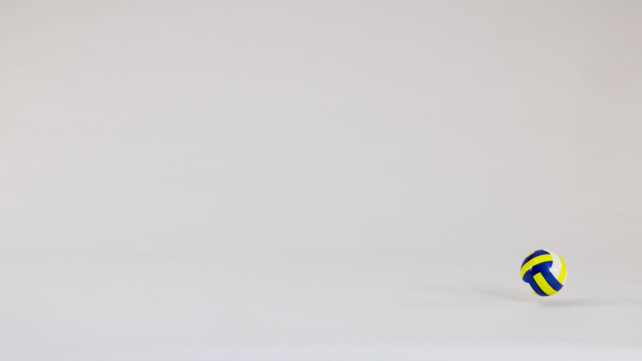 A small yellow and blue volleyball bounces across a clean white studio background in slow-motion