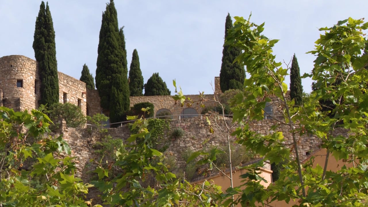 Inquadratura dal basso di antiche mura in pietra e cipressi sotto un cielo sereno