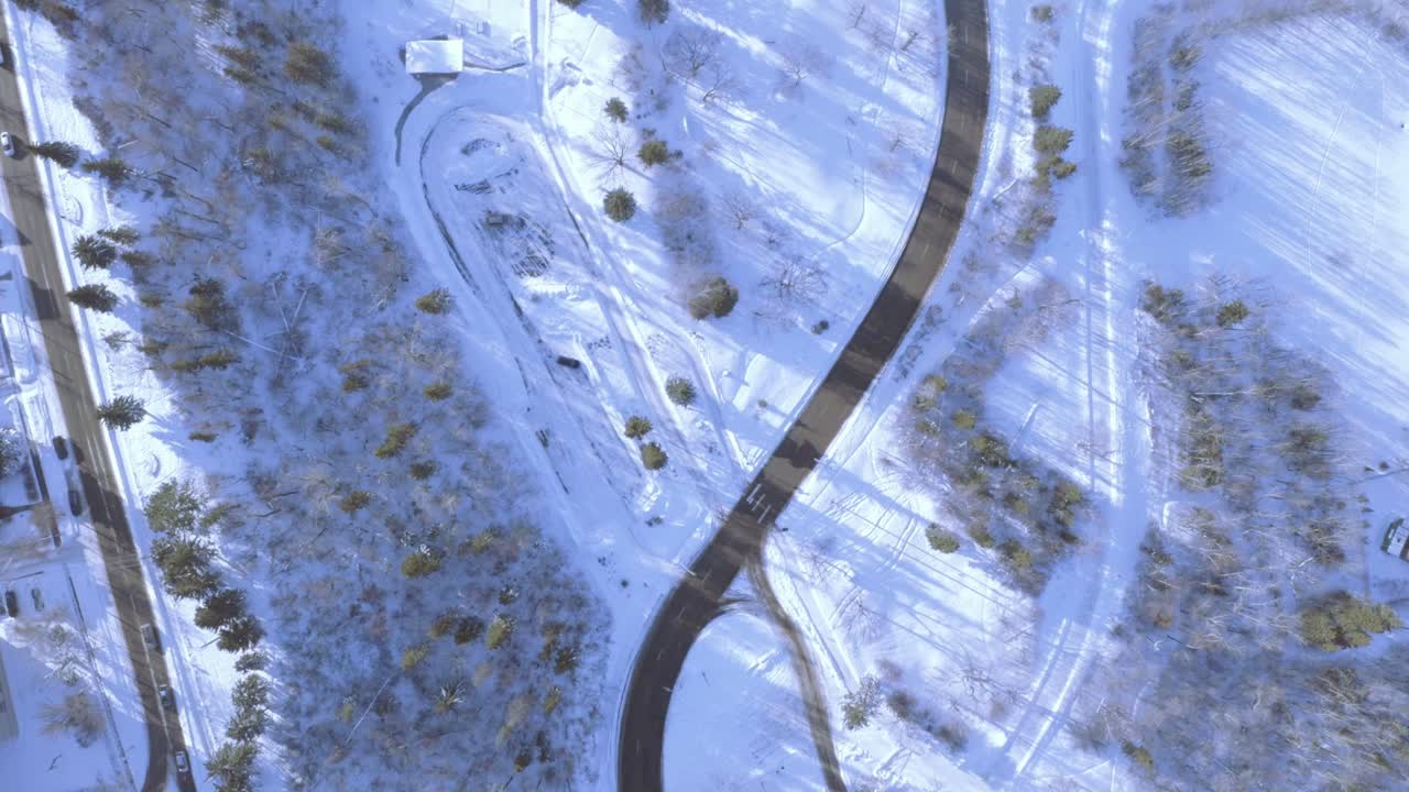 Winter Birds eye view aerial dizzy spiral in altitude at a town with light traffic that connects to a highway next to a park and emergency road options for assistance.