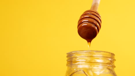 honey dripping from wooden dipper into jar