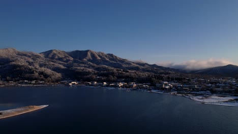 Pequeña-Ciudad-Japonesa-Junto-Al-Lago-Con-Colinas-Cubiertas-De-Nieve-En-Invierno