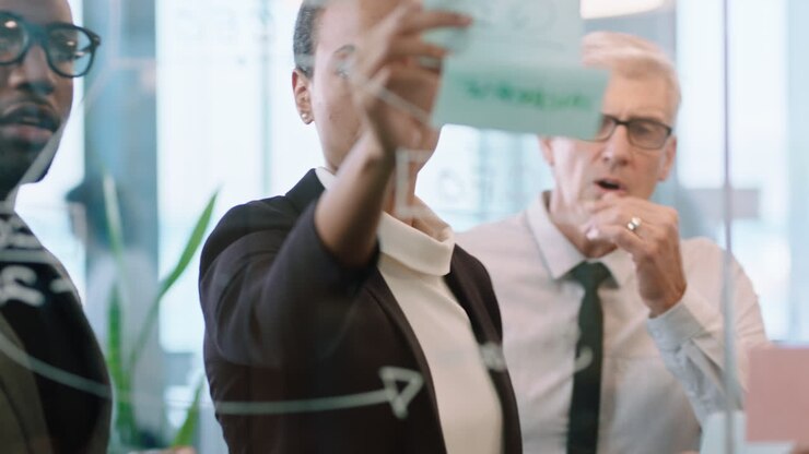 business team meeting using sticky notes writing on glass whiteboard brainstorming colleagues working on problem solving strategy thinking of solution for project in office