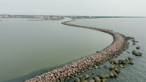 aerial establishing view of port of liepaja concrete pier, baltic sea coastline , distant liepaja city cityscape, overcast day, moody feeling, calm sea, wide drone shot moving forward