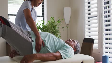 mixed race female physiotherapist helping senior man stretching his legs