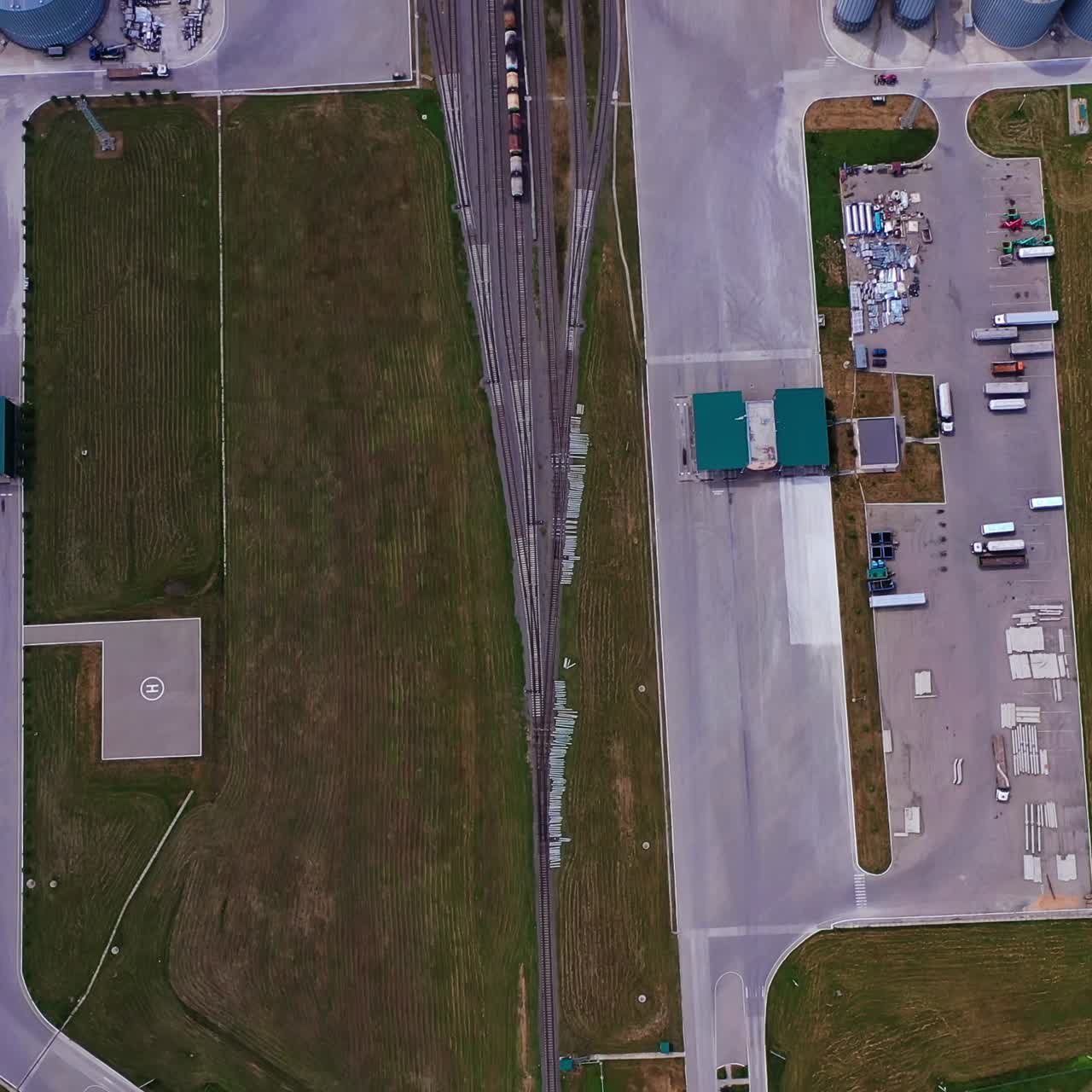 New plant for storing crops locating in the vast field. Huge metal tanks of grain elevators, railways and trains at the territory of the plant. Aerial view