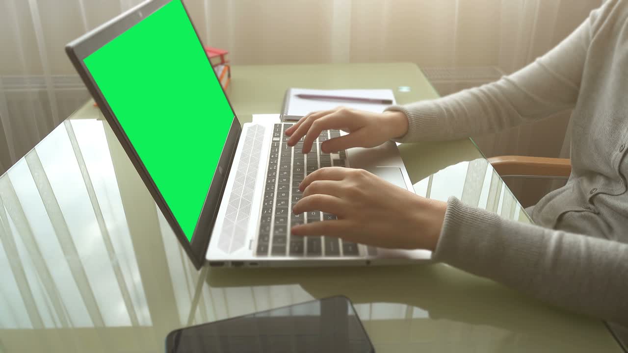 The girl working at home office hands on keyboard. The screen is a green background.