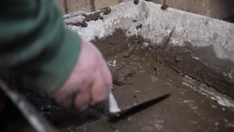 close-up of a hand mixing wet concrete with a trowel in a bucket on a construction site