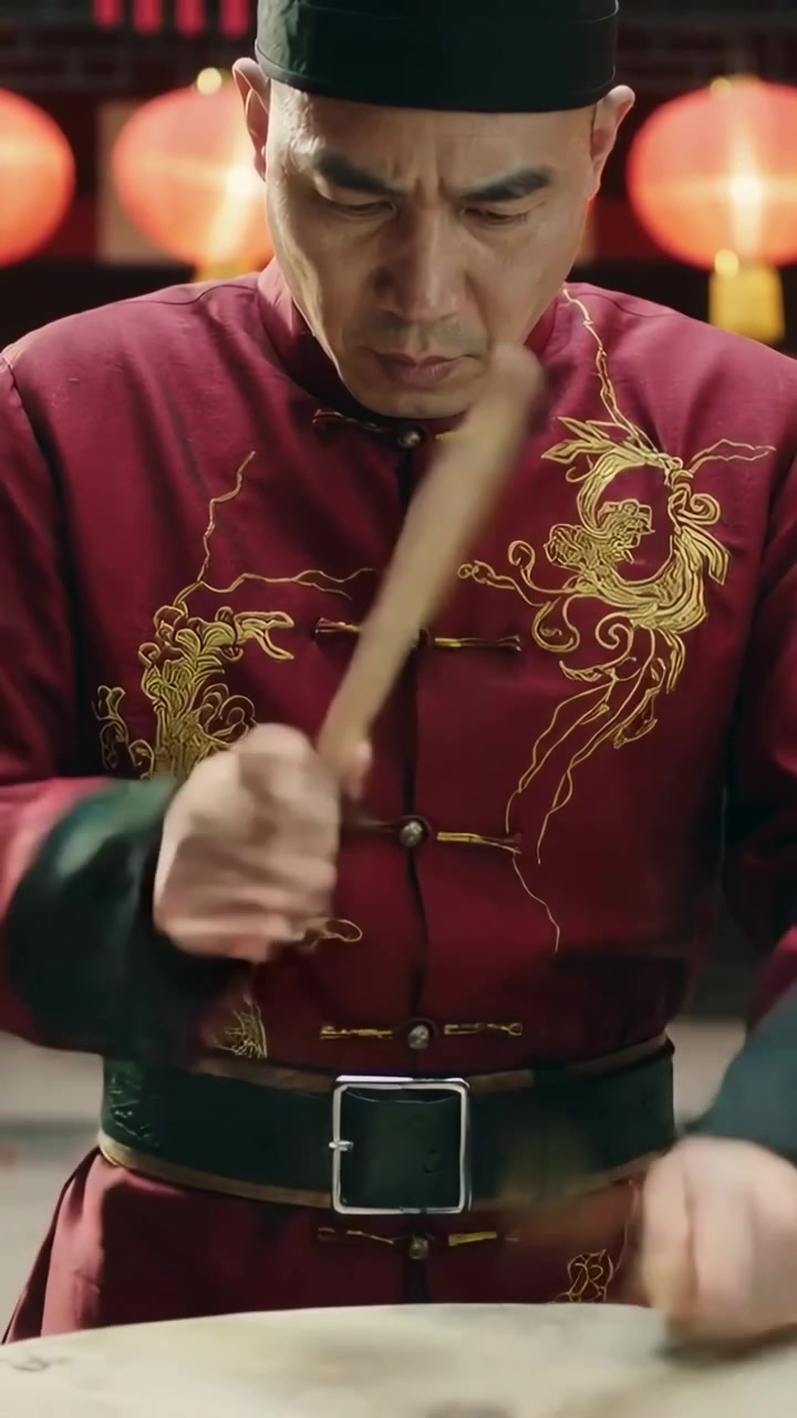 Video vertical: Hombre con chaqueta roja levantando palos de madera y golpeando un tambor para una ceremonia, con faroles.