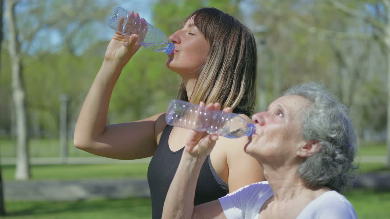 mujeres jóvenes y de mediana edad en el parque bebiendo agua después de correr