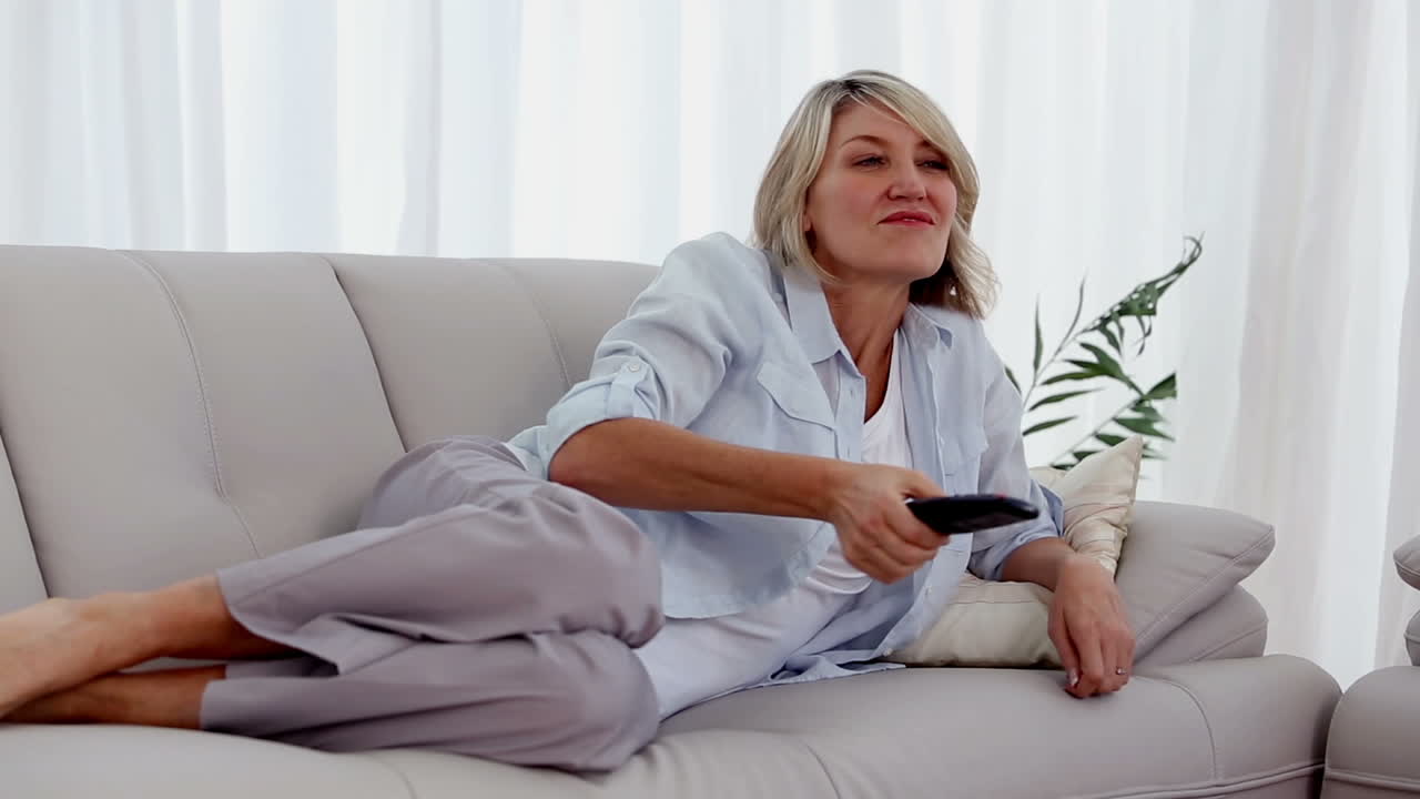Kvinde ligger på sin sofa og ser fjernsyn