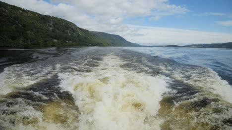 A boat leaves ripples on a calm Scottish lake, surrounded by lush hills and blue skies