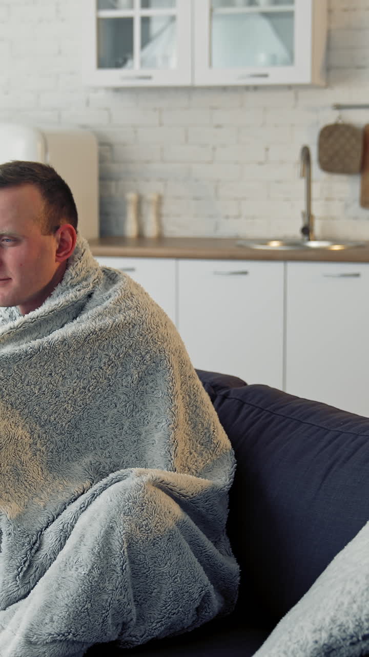 Unwell guy suffering coronavirus infection. Sick man with feeling ill and laying down on bed wrapped in blanket. Vertical video