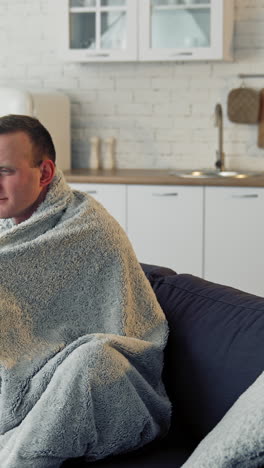 unwell guy suffering coronavirus infection. sick man with feeling ill and laying down on bed wrapped in blanket. vertical video