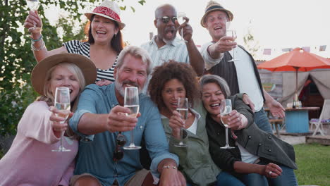 portrait of mature friends sitting around fire and making a toast at outdoor campsite bar