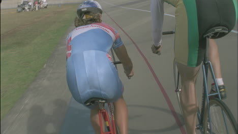 a man and woman ride bicycles around a track