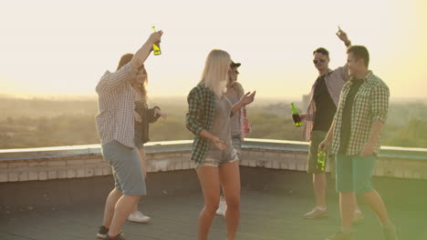 a company of six young people threw a party with beer. russian girl is dancing on the roof with her friends on the teamy party. she dances in denim shorts and green plaid shirts.