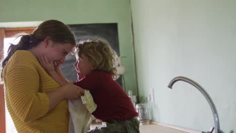 happy caucasian mother and son playing and embracing in kitchen