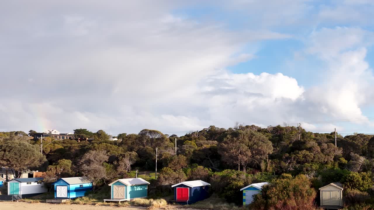 Daytime camera pan reveals vibrant beach huts, coastal vegetation, and dramatic sky in natural light