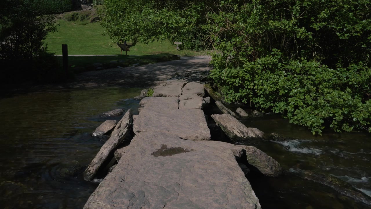 A steady shot capturing Tarr Steps in Exmoor National Park, showcasing the ancient clapper bridge stretching across the gently flowing River Barle.