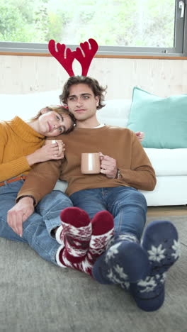 vertical video: relaxing at home, couple enjoying hot drinks with festive socks and antlers