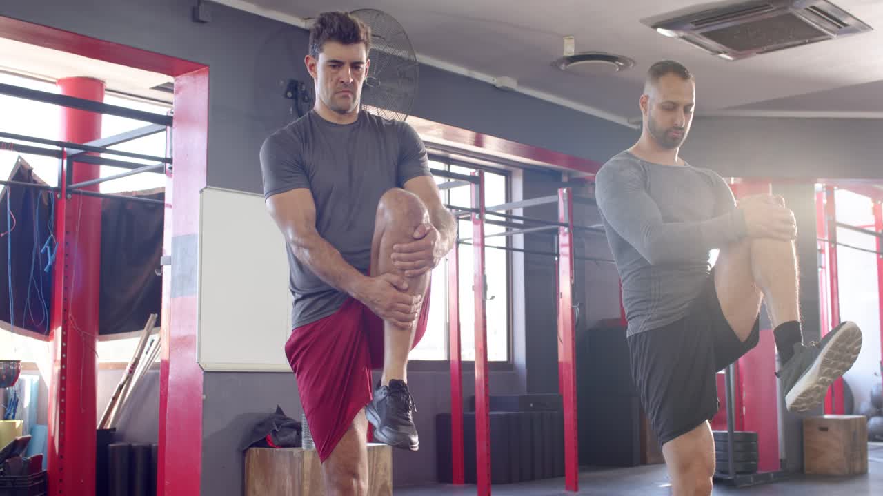 Diversos compañeros masculinos realizando estiramientos alternos de rodilla al pecho en el gimnasio cerca de un cajón pliométrico.