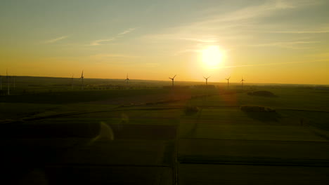 wind farm in green fields silhouettes on sunset in puck poland, aerial drone