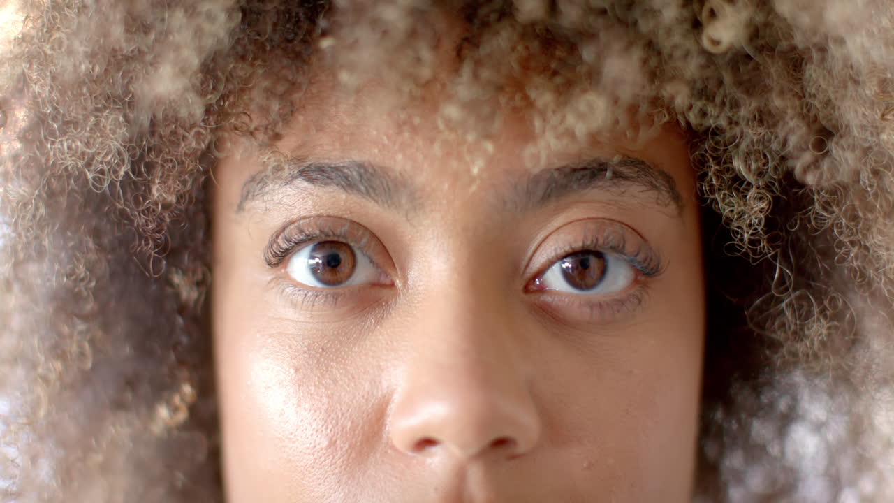 Close-up of person with curly hair looking directly at camera, serious expression