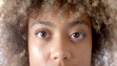 close-up of person with curly hair looking directly at camera, serious expression