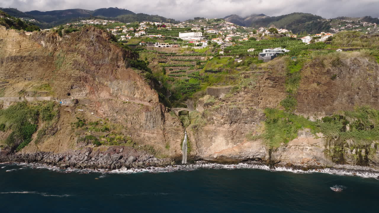 Vista aerea di una cascata costiera che si getta nell'oceano con un villaggio sulle scogliere.