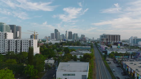 Forwards-fly-above-town-development,-high-rise-apartment-buildings-in-background.-Railway-track-leading-through-city.-Miami,-USA