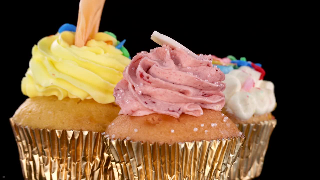 Three colorful cupcakes with sprinkles rotate on a black background under bright studio lighting