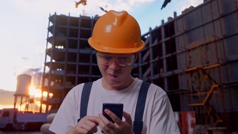 un trabajador asiático mirando un teléfono inteligente y luego celebrando en el sitio de construcción