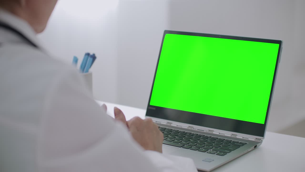 la médica está consultando en línea, mirando la pantalla verde de la computadora portátil para la tecnología de llave cromática, escuchando y respondiendo, gesticulando con las manos