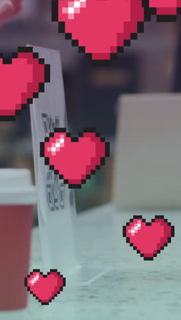 múltiples iconos de corazón rosa flotando contra una persona que hace un pago a través de un teléfono inteligente en una cafetería