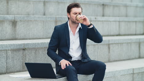 businessman typing on laptop computer on street. man drinking take away coffee