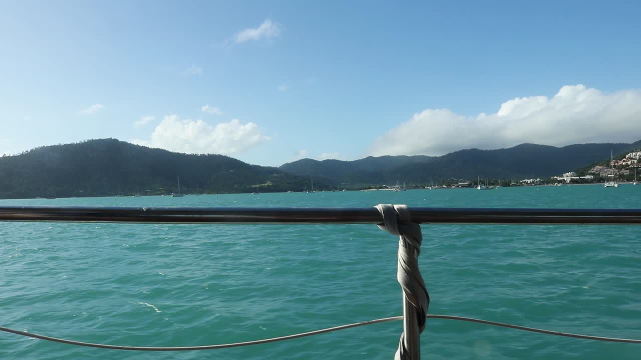 Reling eines Segelboots mit Blick auf den blauen Ozean und tropisches Land.