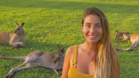 girl smiling at the camera while sitting on the grass with eastern grey kangaroos - gold coast, queensland, australia