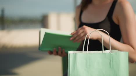 close-up of a woman retrieving a mint-colored book from a matching mint green shopping bag, she flips through the pages, with her upper body slightly blurred in the background