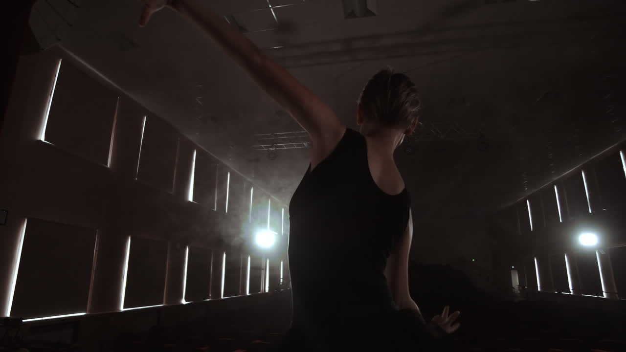 SLOW MOTION: Ballerina dancing in Pointe shoes on stage in smoke in the dark light back view. the camera moves on gimbal