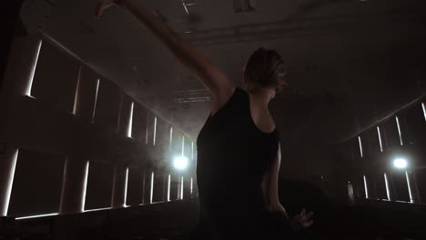 movimiento lento: bailarina bailando en zapatos de punta en el escenario en el humo en la luz oscura vista trasera. la cámara se mueve en gimbal